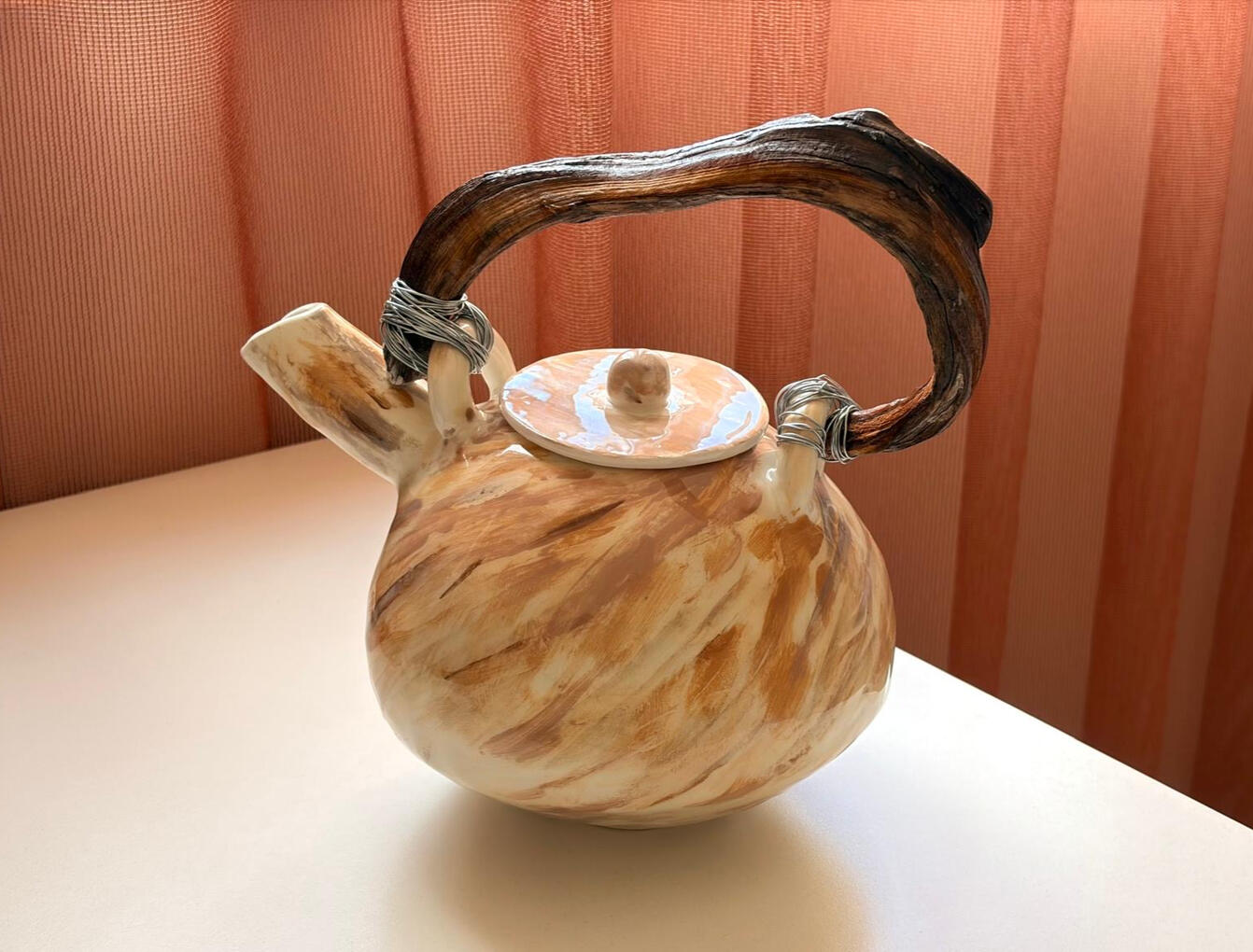 A handcrafted ceramic teapot with a natural wood handle and sculptural wire wrapping, featuring a marbled beige glaze and soft organic form. This piece blends clay, wood and metal into a warm, rustic, wabi‑sabi inspired design. Perfect for lovers of artisa